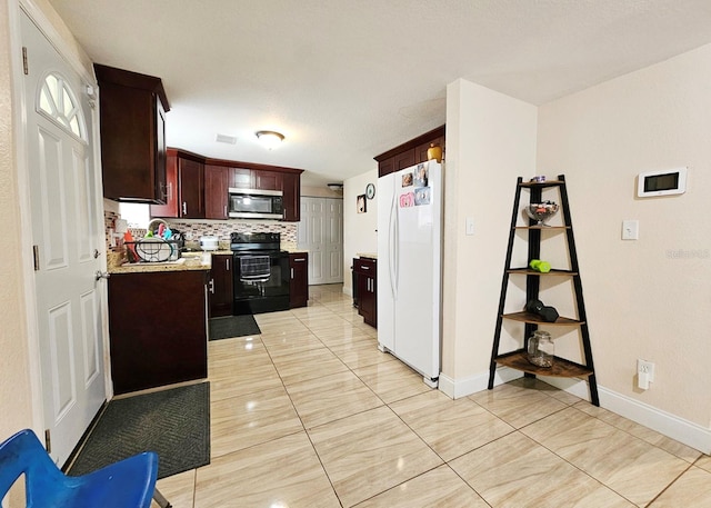 kitchen with light stone countertops, black electric range oven, backsplash, white fridge, and light tile patterned flooring