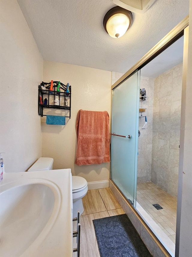 bathroom featuring hardwood / wood-style floors, a textured ceiling, toilet, and a shower with door