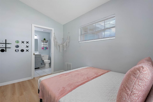 bedroom featuring ensuite bath, light hardwood / wood-style flooring, and lofted ceiling