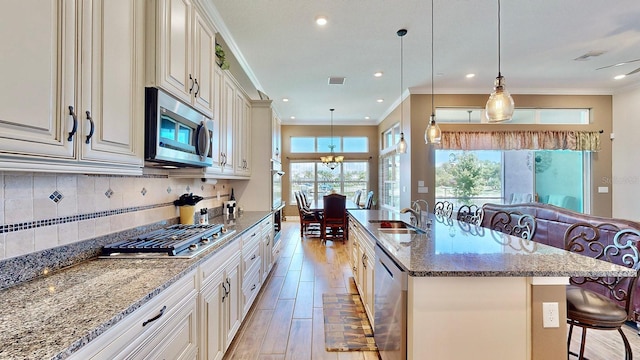 kitchen with stone counters, sink, stainless steel appliances, decorative light fixtures, and a kitchen bar