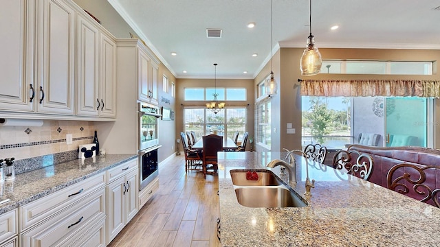 kitchen with light stone countertops, tasteful backsplash, sink, pendant lighting, and an inviting chandelier