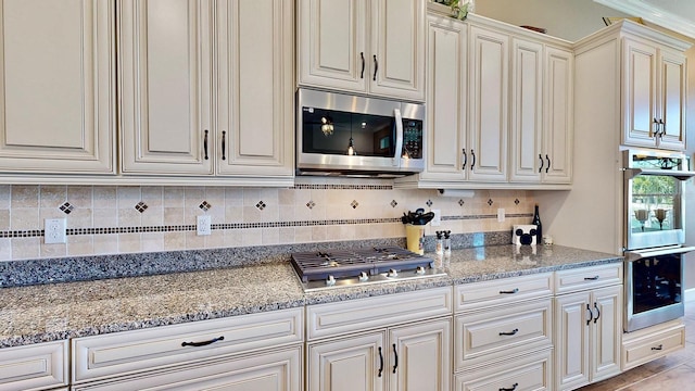 kitchen with backsplash, cream cabinets, crown molding, light stone countertops, and stainless steel appliances