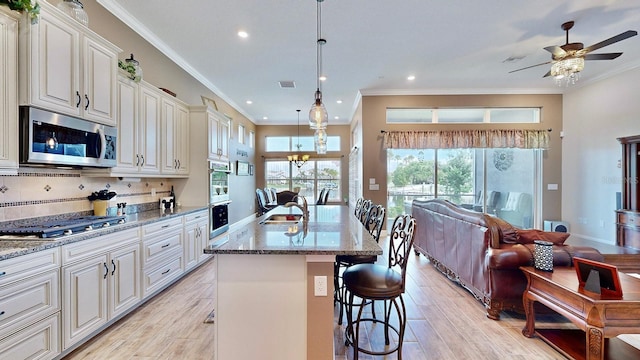 kitchen with hanging light fixtures, stainless steel appliances, a kitchen breakfast bar, decorative backsplash, and a center island with sink