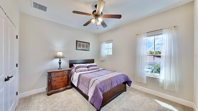 bedroom with multiple windows, ceiling fan, a closet, and light colored carpet