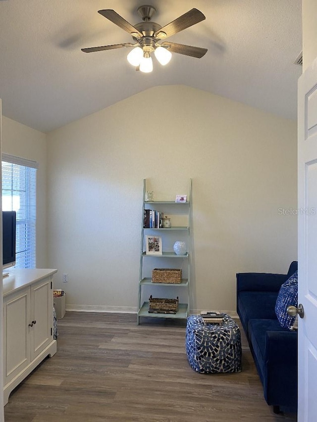 living area with ceiling fan, dark hardwood / wood-style flooring, and vaulted ceiling