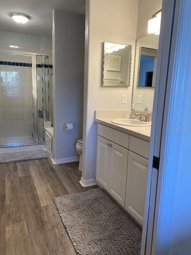 bathroom featuring hardwood / wood-style floors, vanity, toilet, a textured ceiling, and a shower with shower door