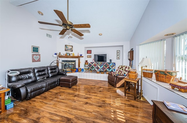 living room featuring wood-type flooring, vaulted ceiling, ceiling fan, and a tiled fireplace