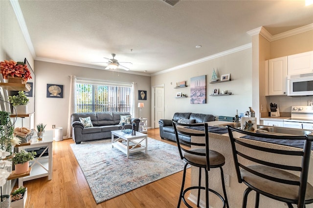 living room featuring a textured ceiling, light wood-type flooring, ceiling fan, and crown molding