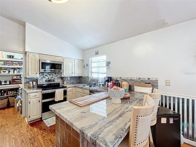 kitchen with decorative backsplash, stainless steel appliances, vaulted ceiling, sink, and cream cabinetry