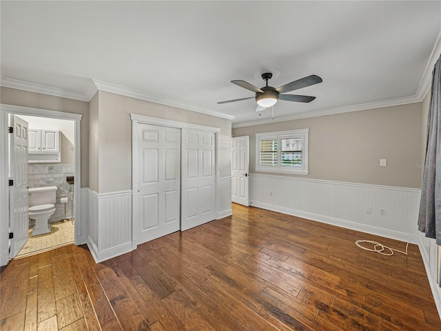 unfurnished bedroom with connected bathroom, ceiling fan, dark hardwood / wood-style floors, crown molding, and a closet