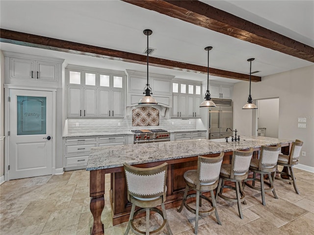 kitchen featuring high quality appliances, a large island with sink, hanging light fixtures, tasteful backsplash, and beamed ceiling