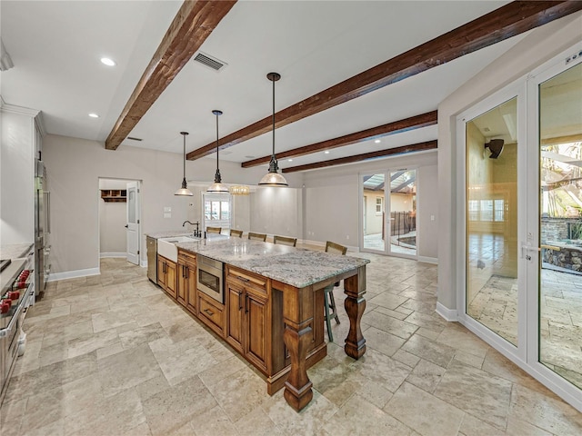 kitchen with a kitchen island with sink, appliances with stainless steel finishes, beamed ceiling, decorative light fixtures, and light stone counters