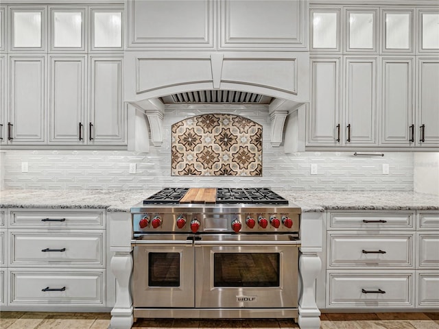 kitchen with light stone countertops, decorative backsplash, white cabinets, and double oven range