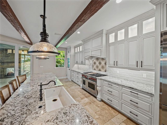 kitchen featuring sink, beamed ceiling, backsplash, range with two ovens, and decorative light fixtures