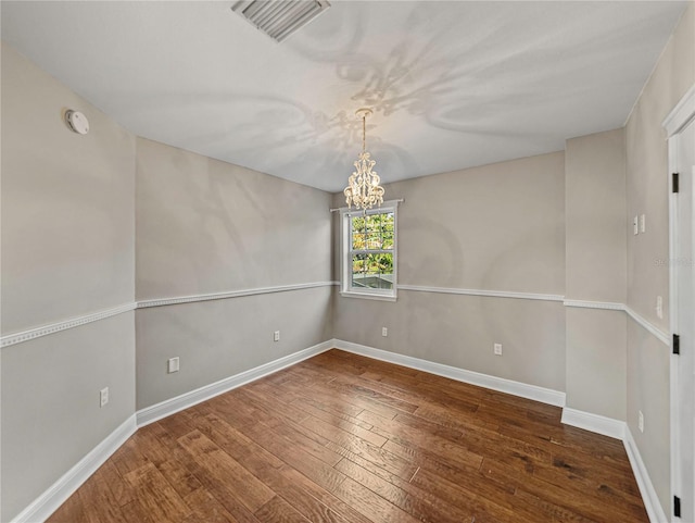 spare room with dark hardwood / wood-style floors and an inviting chandelier