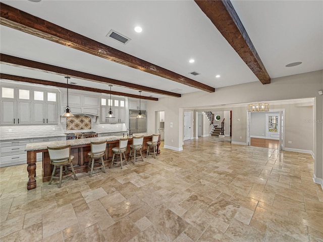 kitchen featuring light stone countertops, an island with sink, decorative light fixtures, beam ceiling, and a breakfast bar area