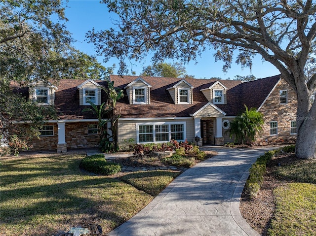 new england style home with stone siding, driveway, and a front lawn