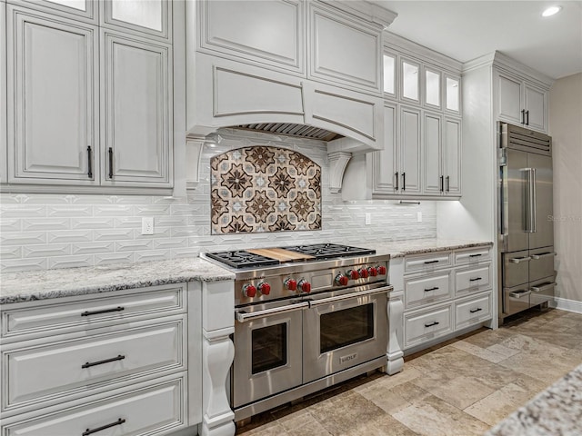 kitchen with high quality appliances, premium range hood, white cabinets, decorative backsplash, and light stone countertops