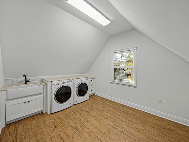 clothes washing area with cabinets, washing machine and dryer, light hardwood / wood-style flooring, and sink