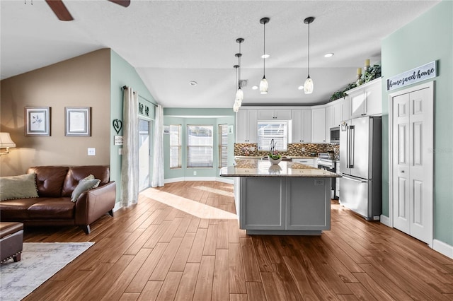 kitchen with a center island, stainless steel appliances, pendant lighting, lofted ceiling, and white cabinets