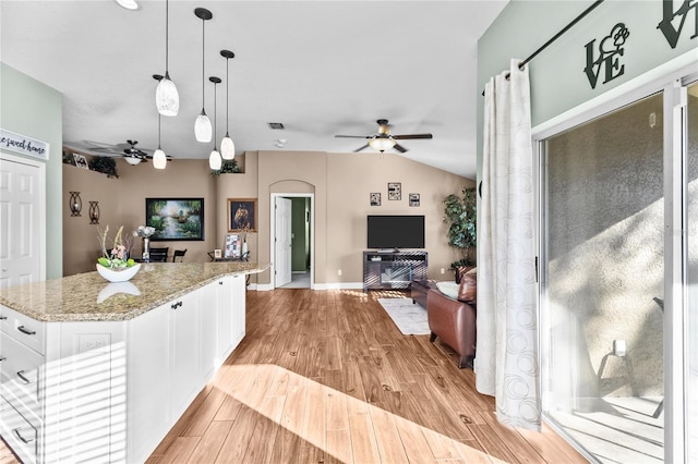 kitchen with light stone counters, decorative light fixtures, white cabinets, a center island, and light hardwood / wood-style floors