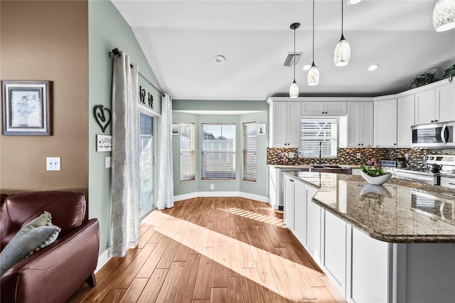 kitchen with white cabinetry, light hardwood / wood-style flooring, dark stone counters, decorative light fixtures, and appliances with stainless steel finishes