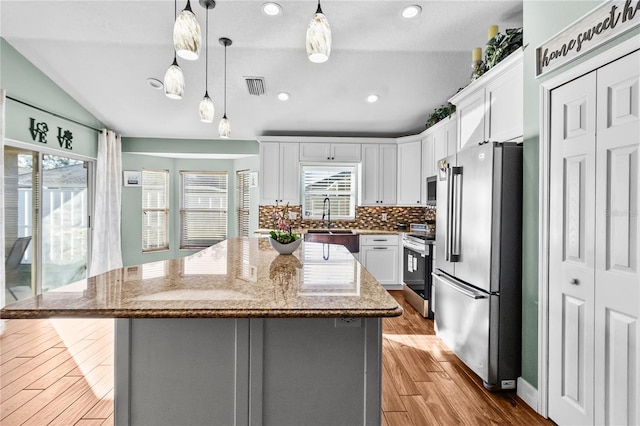 kitchen featuring a center island, lofted ceiling, appliances with stainless steel finishes, light stone counters, and white cabinetry