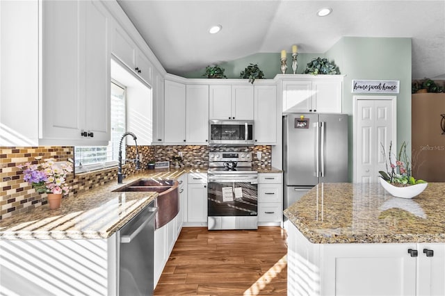 kitchen featuring decorative backsplash, appliances with stainless steel finishes, stone counters, white cabinetry, and lofted ceiling