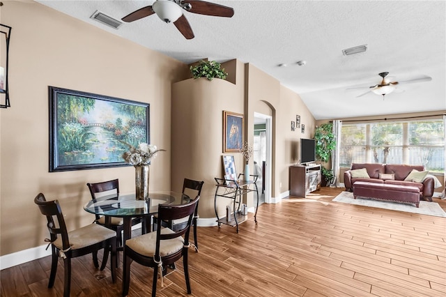 dining space with a textured ceiling, light hardwood / wood-style floors, ceiling fan, and lofted ceiling