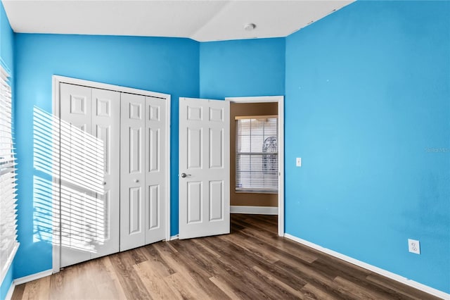 unfurnished bedroom featuring a closet, wood-type flooring, multiple windows, and vaulted ceiling