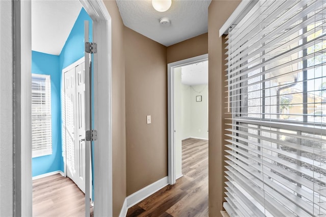 hallway with a textured ceiling, hardwood / wood-style floors, and vaulted ceiling