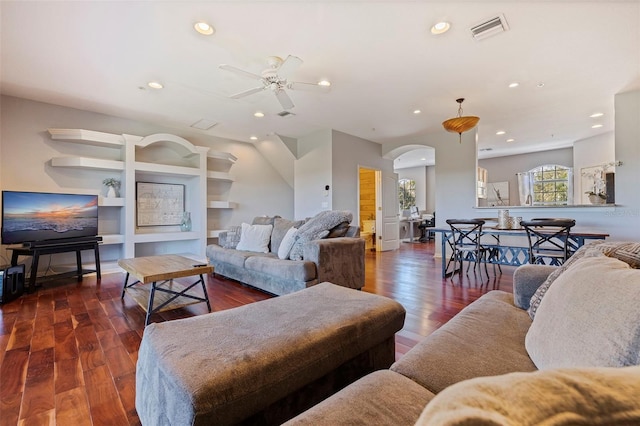 living room with built in shelves, ceiling fan, and dark wood-type flooring