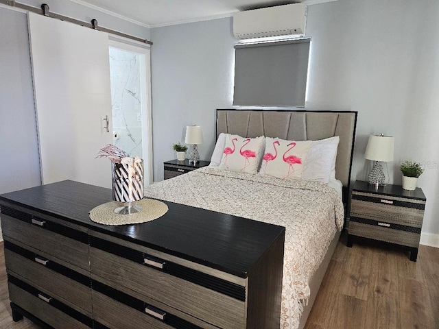 bedroom featuring hardwood / wood-style floors, a barn door, ornamental molding, and a wall unit AC