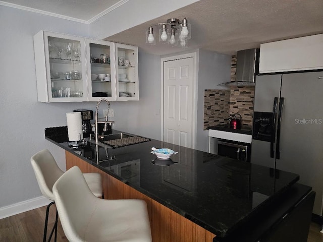 kitchen with white cabinetry, sink, wall chimney exhaust hood, stainless steel fridge with ice dispenser, and kitchen peninsula