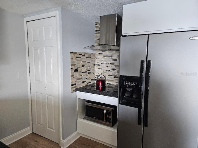 kitchen with dark wood-type flooring, stainless steel appliances, wall chimney range hood, a textured ceiling, and decorative backsplash