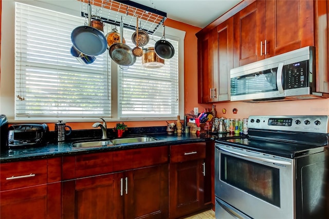 kitchen with stainless steel appliances, dark stone countertops, and sink