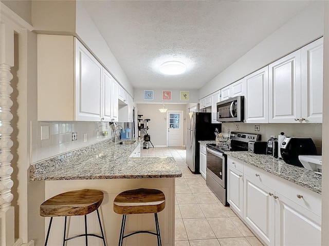 kitchen featuring white cabinetry, kitchen peninsula, a kitchen bar, light tile patterned floors, and appliances with stainless steel finishes