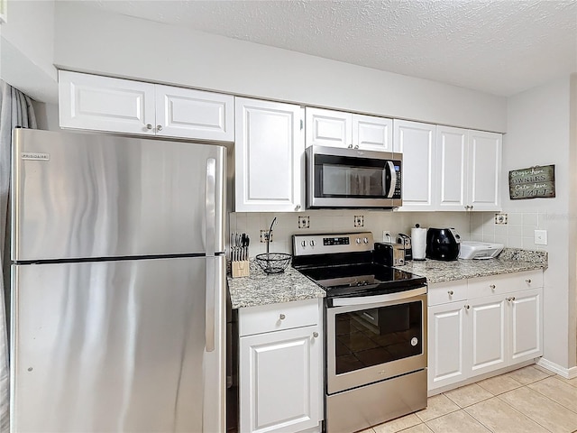 kitchen featuring backsplash, a textured ceiling, stainless steel appliances, light tile patterned floors, and white cabinets