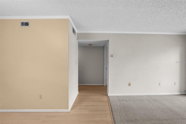 empty room featuring ornamental molding, light hardwood / wood-style floors, and a textured ceiling