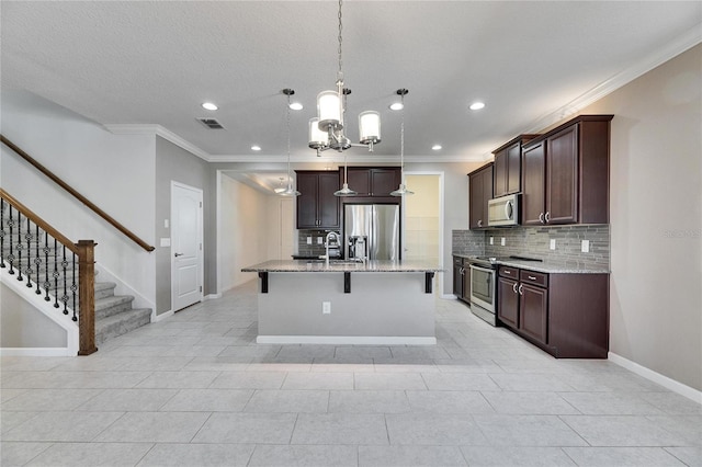 kitchen featuring a center island with sink, appliances with stainless steel finishes, light stone counters, decorative backsplash, and decorative light fixtures