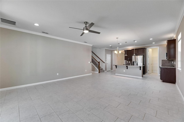 unfurnished living room featuring ceiling fan with notable chandelier, light tile patterned floors, crown molding, and sink