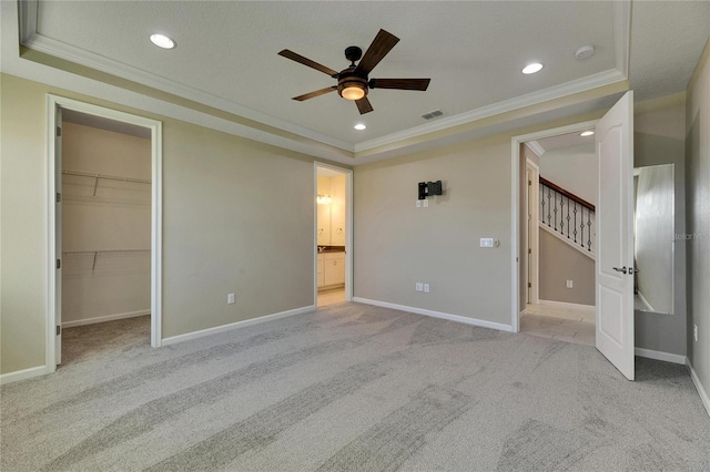 unfurnished bedroom featuring light colored carpet, crown molding, ceiling fan, a tray ceiling, and a walk in closet