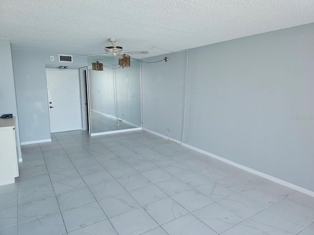 empty room with marble finish floor, visible vents, ceiling fan, a textured ceiling, and baseboards