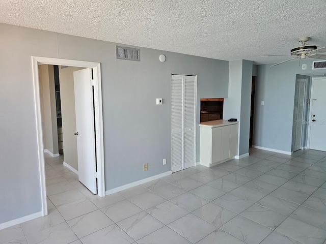 empty room with ceiling fan, a textured ceiling, visible vents, baseboards, and marble finish floor