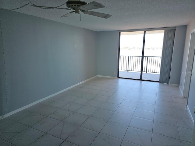 spare room with light tile patterned floors, a ceiling fan, a textured ceiling, a wall of windows, and baseboards