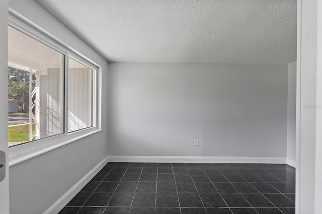 unfurnished room with a wealth of natural light, dark tile patterned floors, and a textured ceiling