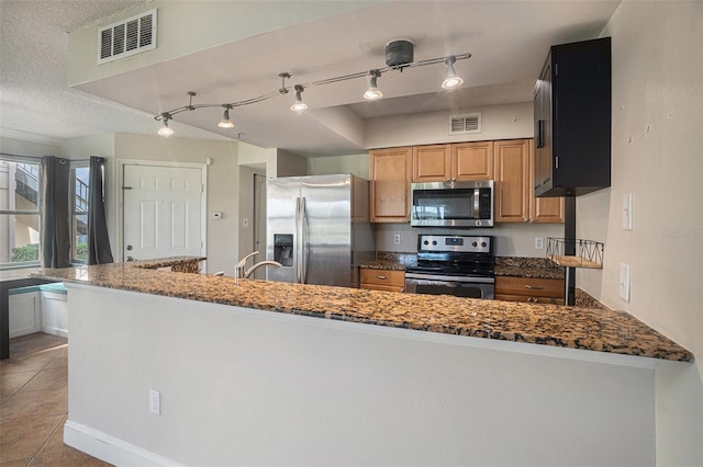 kitchen featuring kitchen peninsula, appliances with stainless steel finishes, light tile patterned flooring, and dark stone countertops