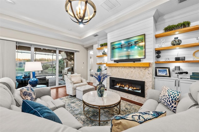 living room featuring hardwood / wood-style floors, crown molding, a chandelier, and a fireplace