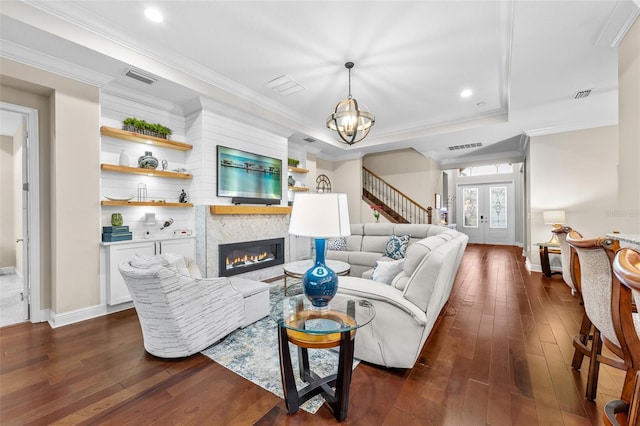 living room with a tray ceiling, a notable chandelier, a large fireplace, french doors, and ornamental molding