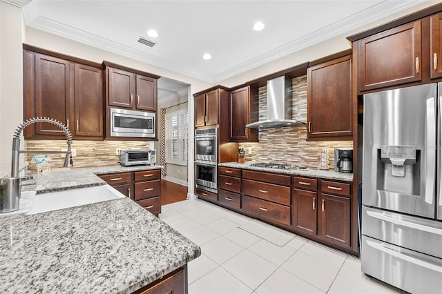 kitchen featuring stainless steel appliances, tasteful backsplash, wall chimney range hood, light stone counters, and sink